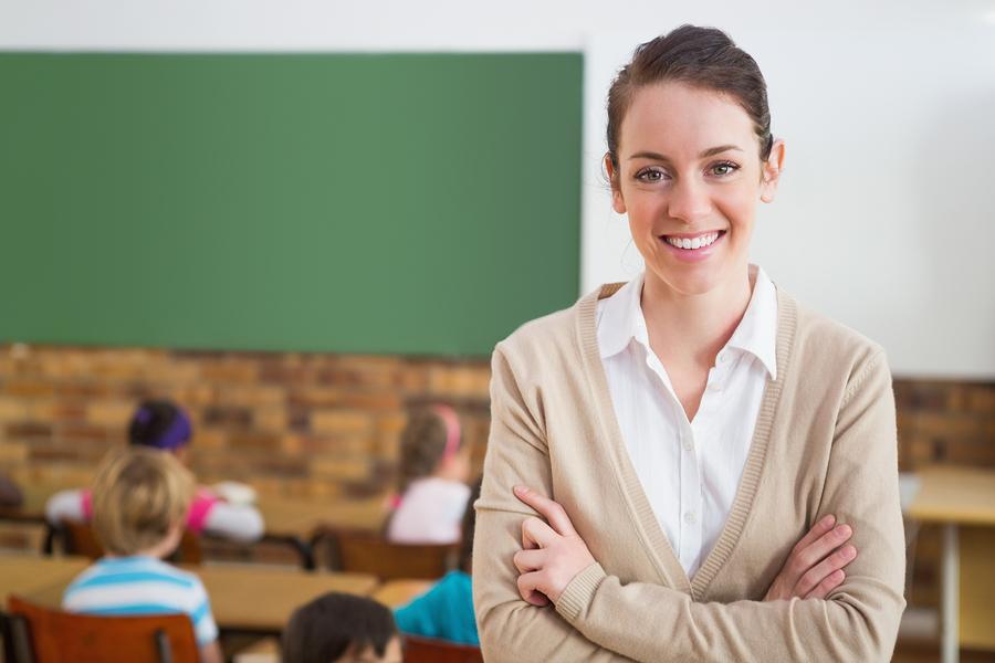 Image of Girl standing in a Classroom having green board and many Students